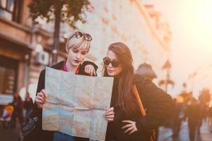 Two young female traveler standing on the street and looking at the map