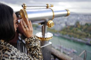 Woman looking through telescope at city from rooftop